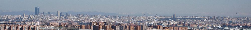 Panorama urbano de Madrid desde 15 km al sur, concretamente desde la cima del Cerro Buenavista. En la izquierda de la imagen aparecen los complejos de rascacielos de Cuatro Torres Business Area (CTBA), Puerta de Europa de Madrid y AZCA. En la derecha se ve el parque del Retiro y a su derecha Torrespaña. Al fondo, los Montes Carpetanos o Sierra de Guadarrama, en el Sistema Central, a espaldas de la ciudad.