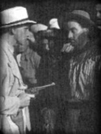 El capanga (Francisco Petrone) apunta con un arma al mensú (Ángel Magaña).