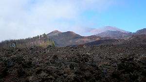 Volcán Chinyero. En primer término, campos de lavas de sus erupciones. Al fondo, entre nubes, los volcanes Teide y Pico Viejo.