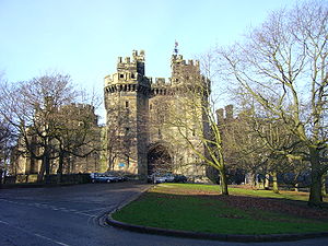 View down a short tree-lined drive leading to the main entrance of a castle, which is flanked by two tall towers.